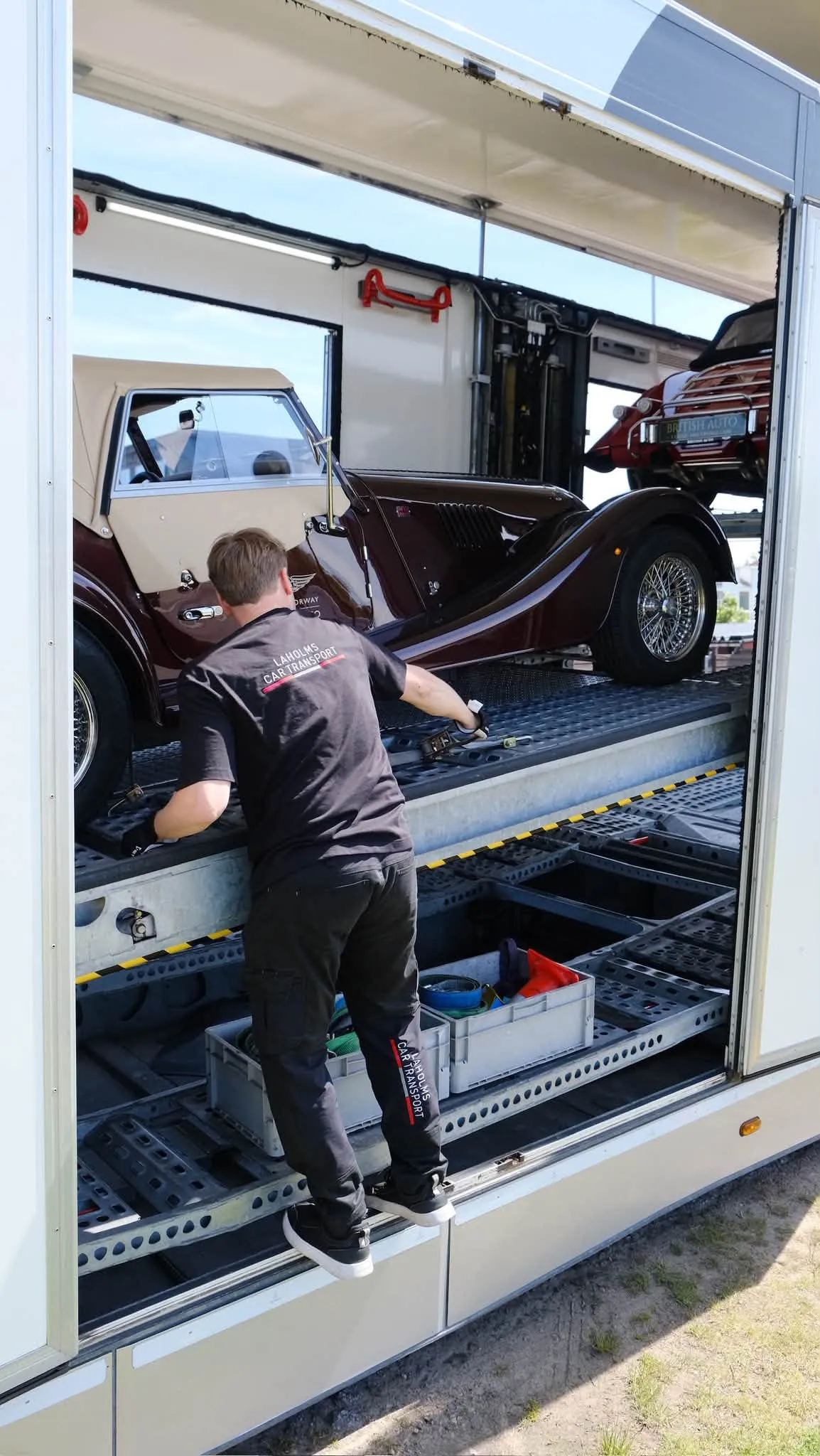 A driver straps down a Morgan on the upper deck of the trailer